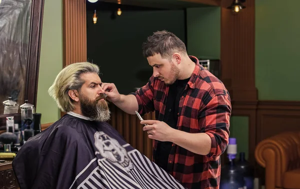 Kendini talep et. Kuaförde olgun bir adam. Saç bakımı ve erkek bakım konsepti. Formunu koru. Sakallı adam berbere sakal tıraşı oluyor. Bıyık ve sakal. Kuaförde sandalyede oturuyor.