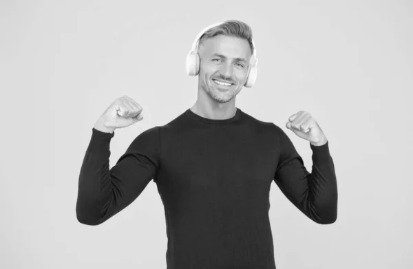 Bonito homem feliz ouvir música em fones de ouvido elegantes no fundo amarelo, tecnologia moderna — Fotografia de Stock