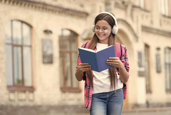 Felice bambino moderno leggere libro ascoltare audio corso di lingua in cuffie all'aperto, inglese, spazio copia — Foto Stock