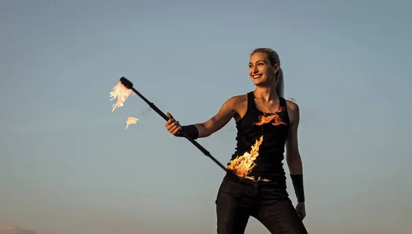 Happy sexy fire performer woman manipulate flaming baton on blue sky outdoors, performance
