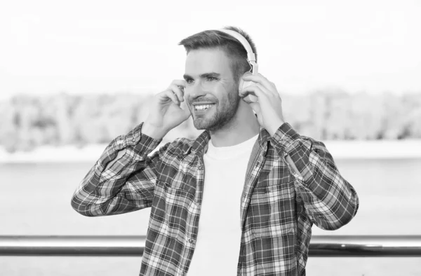smiling bearded man listen music in digital earphones wearing checkered shirt outdoor, technology