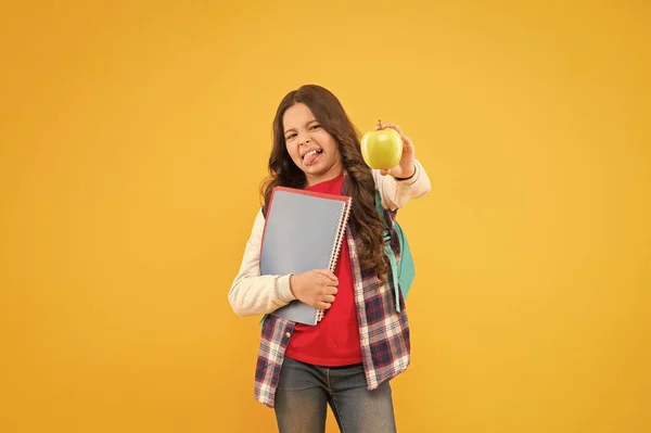 Äpplet är slut nu. Små barn gör ansiktet håller äpple och böcker gul bakgrund. Surt äpple. Ett mellanmål i vitaminskolan. Hälsosam mat och kost. Ekologisk och naturlig mat. Hälsoutbildning — Stockfoto