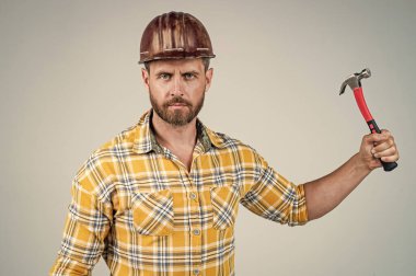 İnşaat kaskı ve inşaat alanında çekiçle, alet edevat dükkanıyla kareli gömlek giyen yakışıklı bir adam.