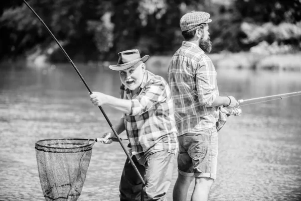 Siente el engranaje. padre e hijo pescando. pasatiempo y actividad deportiva. Cebo para truchas. fin de semana de verano. hombres maduros pescador. dos pescador feliz con caña de pescar y red. amistad masculina. vinculación familiar —  Fotos de Stock