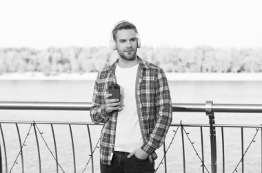 Kahve fincanı açık havada traşsız bir adam. Gündelik erkek hippi modası. Kulaklıklı adam, dinle. Müzik tarzı. Kahve içerken para kazanmak. Ses kalitesi. Günaydın içecek.