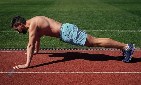 Sportowy człowiek robi pompki stojąc na desce na zewnątrz stadionu, sport — Zdjęcie stockowe