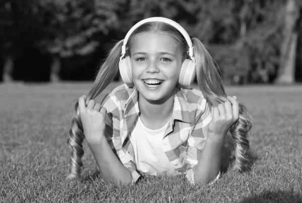 Naucz się każdego języka w zabawny sposób. Szczęśliwy dzieciak nosi słuchawki leżące na zielonej trawie. Kursy języka obcego. Angielska szkoła. Prywatna lekcja. Nieformalna edukacja. Program audio. Kształcenie na odległość — Zdjęcie stockowe