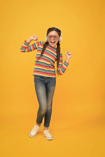 Ευτυχισμένο κορίτσι έφηβος φορούν μοντέρνα ακουστικά. Αστείο παιδί που ακούει μουσική. ομορφιά σε glamour γυαλιά. Παιδική ευτυχία. χαμογελαστό παιδί σε κίτρινο φόντο. hipster στυλ μόδας κόμμα. Διάδοση γνώσεων — Φωτογραφία Αρχείου