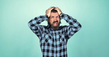 Başım ağrıyor. Modern görünümlü sakallı hippinin başı ağrıyor. Sağlık hizmeti konsepti. Bıyıklı vahşi yakışıklı adam. Mavi arka planda olgun bir berber. Erkeklik ve karizma. Hayır.