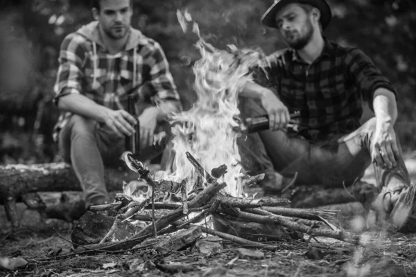 great time together. two men relax at fire. hiking and camping. male friendship. drink beer bonfire. ranger at outdoor activities. spend picnic weekend in nature. Adventure concept. hike and people