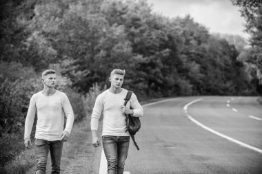 Macera konsepti. Yolda otostop çeken adamlar. Turist gezgini otomobil durağında durur. Taşıma sorunları. Arabanın kolayca kenara çekebileceği bir yer seç. Erkekler sırt çantasıyla yürüme yolu. İkizler yol boyunca yürür