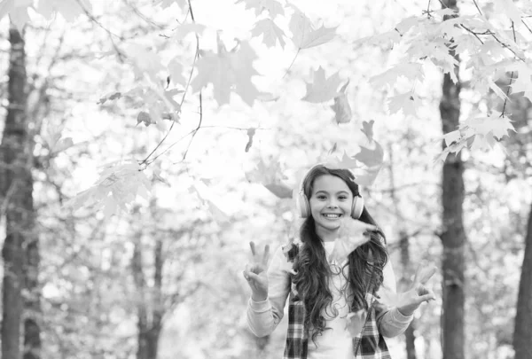 Χαρούμενο κορίτσι σε casual στυλ περνούν το χρόνο τους στο φθινόπωρο δάσος με φύλλα σφενδάμου απολαμβάνοντας καλό καιρό ακούγοντας μουσική στα ακουστικά, ευτυχισμένη παιδική ηλικία — Φωτογραφία Αρχείου