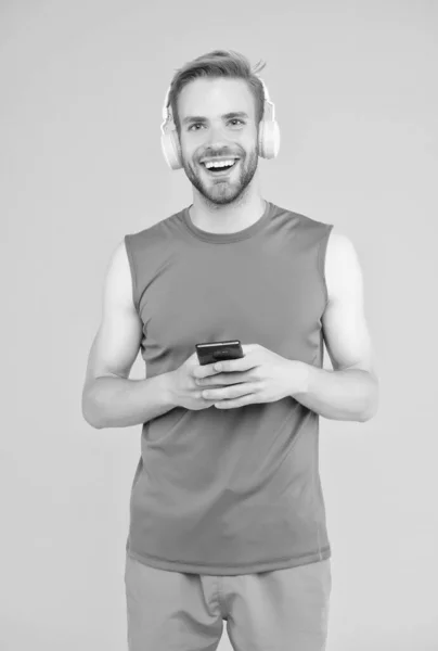 Happy young guy in sportswear wear modern headphones listening music while training use smartphone, fitness shopping app — Stock Photo, Image