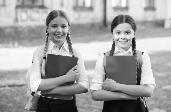 Divirta-se enquanto estuda. Meninas felizes em uniforme escolar. Estudantes adolescentes sorridentes com mochila segurando copybook. educação na escola primária. alunas aprendendo assunto juntos — Fotografia de Stock