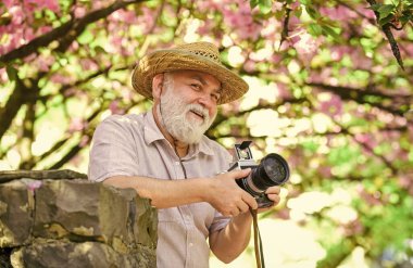 Tamamen rahatla. Turist, kamera kullanarak kiraz çiçeklerinin fotoğrafını çeker. Çiçek fotoğrafçılığında sakura. Yaşlı sakallı adam pembe çiçeklerin fotoğrafını çekiyor. Profesyonel fotoğrafçı tasarımcısı. Mutlu emeklilik