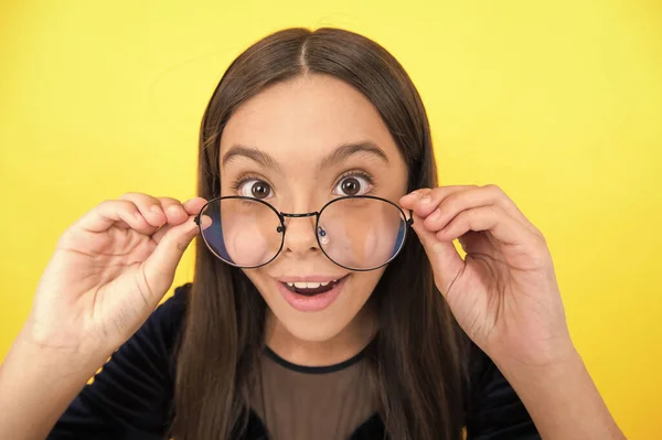Criança menina inteligente surpreso com cabelos longos e óculos no fundo amarelo, surpresa — Fotografia de Stock
