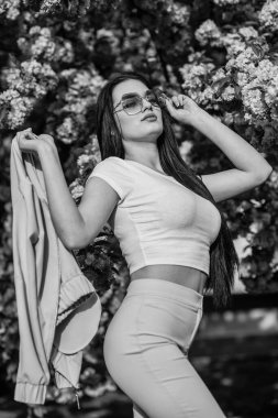 Bahara karşı tutkulu. Kıyafet dükkanı. Açık havada çok güzel bir kız. Bahar çiçeğinin açtığı süslü güneş gözlüklü kadın. Kiraz çiçekli kız. Bahar moda koleksiyonu. Sakura ağacı çiçek açıyor.