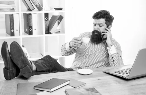 Превосходство в управлении. Менеджер говорит по телефону, пьет чай. Офис-менеджер отдыхает за столом. Использование мобильных технологий. Коммуникации. Современная жизнь — стоковое фото