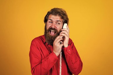 İletişim. Sakallı adam kırmızı gömlek giyer. Sıradan bir erkek telefonu. Sohbet konsepti. Adam sekreter ya da asistan retro telefonda konuşuyor. Telefonlu acımasız adam.