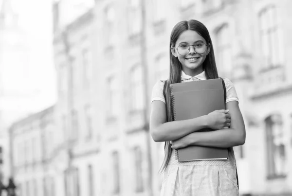 Счастливый маленький ребенок носит очки и школьную одежду, держа учебники на улице, образование, копировальное пространство — стоковое фото