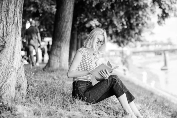 Література для літніх канікул. Літня відпустка. Студентський розумний ботанік сидить на зеленій траві і читає книгу. Дівчина розслабляється на березі річки після робочого дня. Розслабтеся і захоплюйтеся. Жінка мріє про відпустку — стокове фото