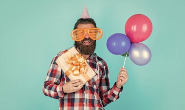 Havalı saç stili olan şık sakallı adam kareli gömlek giyiyor parti balonları ve hediye kutusu, mutluluk.