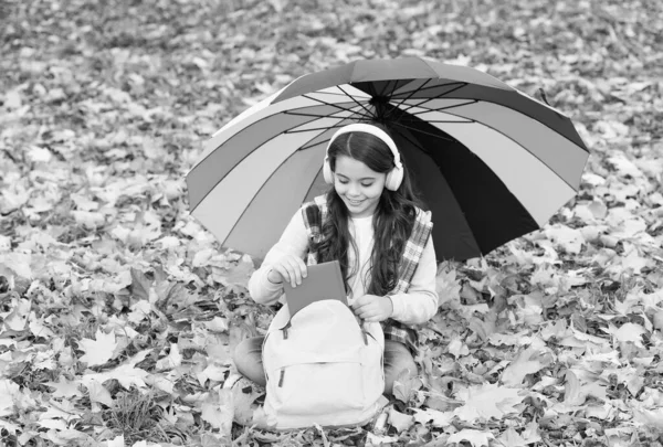 going to read the book. happy childhood. back to school. girl in headset with backpack relax in park. enjoy fall in forest. listen to music. online courses education. autumn kid under umbrella