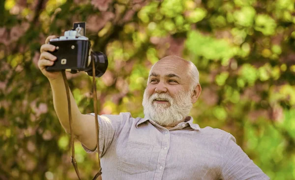 Selfie fixe. designer de fotógrafo profissional. homem turista uso câmera tirar fotos de flores de cerejeira. sakura em plena floração fotografia. Ramo com flores rosa. homem barbudo sênior fotografar — Fotografia de Stock