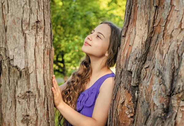 Pequena criança sonhadora com cabelo ondulado longo e beleza olhar sonho no tronco da árvore no parque de verão, futuro — Fotografia de Stock