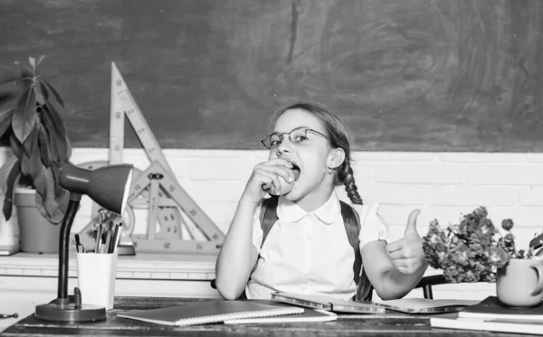 Μαθήτρια κάθεται γραφείο chalkboard φόντο. Μαθητής στο σχολείο. Κορίτσι μικρό παιδί τρώει μήλο σνακ. Σχολικές διακοπές. Χαλάρωσε ανάμεσα στα μαθήματα. Φόρτιση βιταμινών. Σχολική ζωή. Υγιής τρόπος ζωής — Φωτογραφία Αρχείου