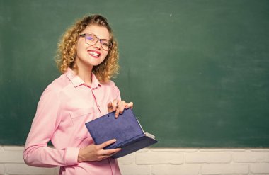 Öğretmen zor konuyu açıkla. Pedagog kitabı tutuyor ve bilgiyi açıklıyor. Eğitim konsepti. Karatahtanın önündeki kadın öğretmen. Öğrencilerin en iyi öğretmeni. Bilgiye karşı tutkulu