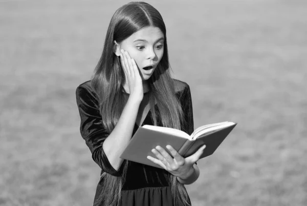 Verrast klein kind met open mond lees schoolboek groen gras zonnige zomer buiten, informatie — Stockfoto