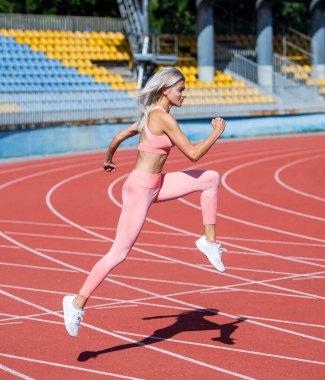Hareket halindeki kadın spor eğitmeni. Hız ve enerji. Dayanıklılık. Spor giyim sektöründe seksi bir koşucu. Açık hava arena pistinde koşuyor. Antrenman ve antrenman. Koşu yapan atletik bayan koç