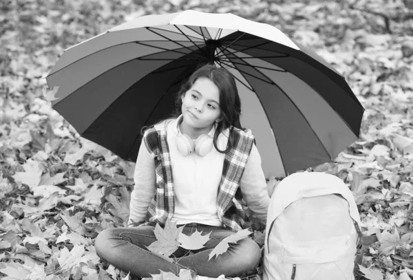 Artık yağmur yok. Sırt çantalı kız yağmur koruması altında. Çocuk sonbahar ormanında rahatlar. Parkta sonbahar yaprakları. Okula dönüyorum. Sıcak mevsimsel havanın tadını çıkar. Mutlu çocuk renkli bir şemsiye altında oturuyor. — Stok fotoğraf