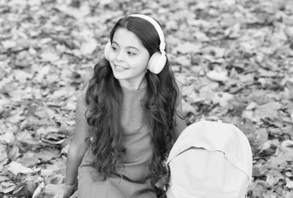 Czas do szkoły. Z powrotem do szkoły. nowoczesna edukacja. dziecko z plecakiem w jesiennym lesie. koncepcja dnia wiedzy. Dzieciak w jesiennym parku. Szczęśliwy dzieciak odpoczywa na jesiennych liściach. mała dziewczynka nosić słuchawki — Zdjęcie stockowe