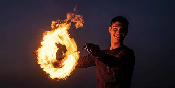 Happy guy artist perform fire ring by spinning burning poi on idyllic dark sky at night outdoors, circle