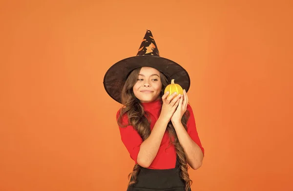 Menina engraçada em chapéu de traje de bruxa para o Halloween com abóbora ou abóbora no fundo laranja, comida halloween — Fotografia de Stock