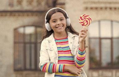 Kablosuz kız kulaklıkları lolipop şekeri yiyor, sevimli çocuk konsepti.