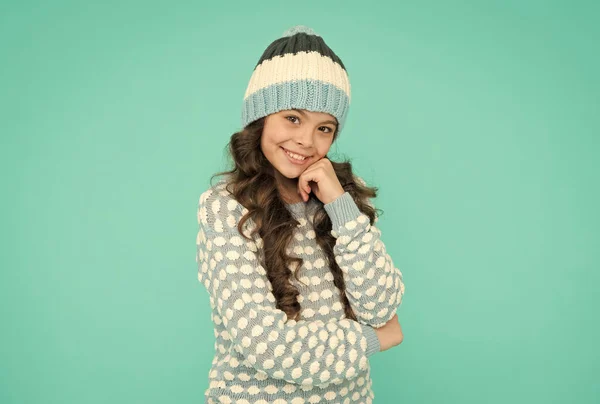 Niña alegre con pelo rizado largo en sombrero de punto y suéter sobre fondo azul, belleza — Foto de Stock