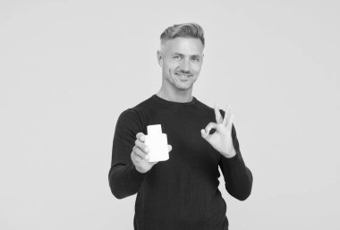 Mutlu yakışıklı adam el hareketini onayla. Kozmetik ürünler sarı arka plan, tamam mı?