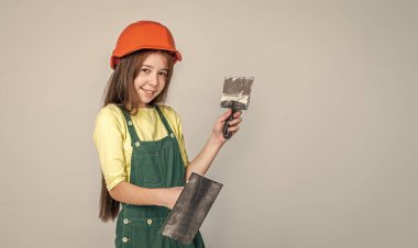 İnşaat alanında şapkalı kız spatula kullanıyor, yardım et.