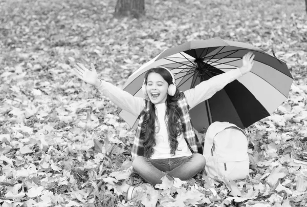 Criança feliz usar fones de ouvido sob guarda-chuva colorido. Menina ouvir música. criança positiva relaxar na floresta de outono. folhas de outono no parque. de volta à escola. educação online. tempo sazonal — Fotografia de Stock