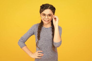 Moda gözlüğü ve modaya uygun gözlükler. Mutlu moda sarı arka plan. Uzun saç örgülü küçük bir çocuk. Sıradan bir tarz. Güzellik ve moda. Moda aksesuarı. Giymek istediğin moda gözlüğü.