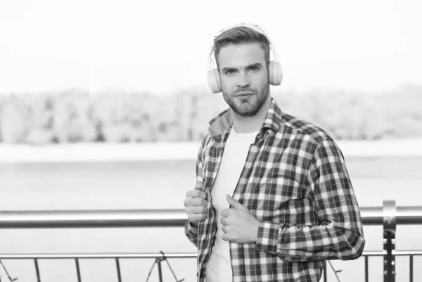 Homem barbudo ouvir música em fones de ouvido digitais vestindo camisa quadriculada ao ar livre, espaço de cópia, estilo casual — Fotografia de Stock