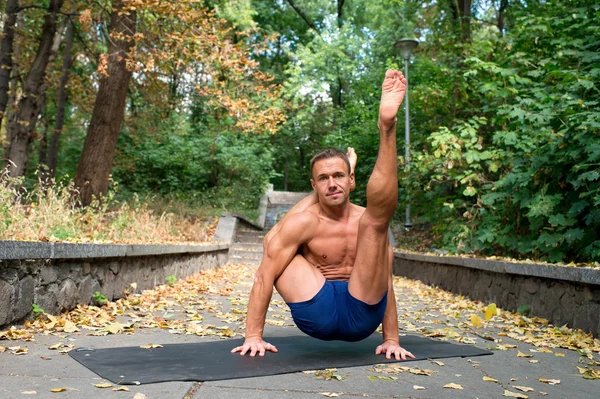 Przystojny sportowiec robi jogi asany w parku — Zdjęcie stockowe