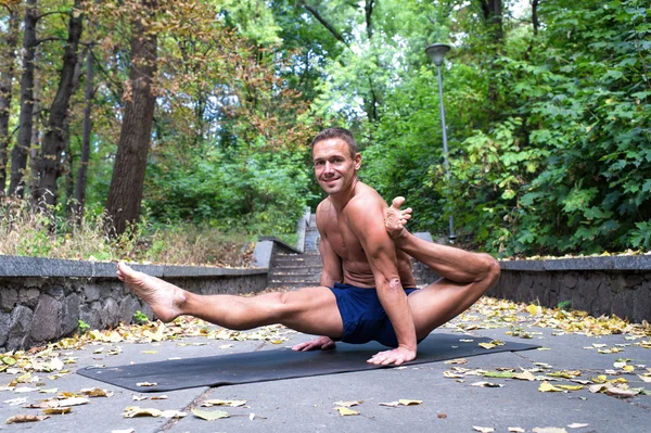 Schöner lächelnder, flexibler, athletischer Mann, der im Park Yoga-Asanas macht — Stockfoto