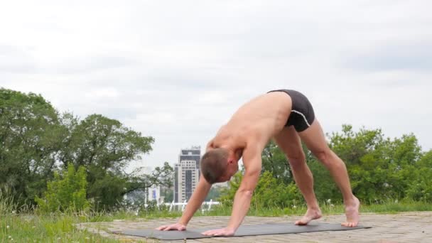 Knappe flexibele atletische man doen yoga asana's in het park — Stockvideo