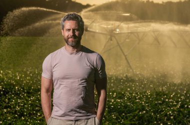 Crop irrigation. Agriculture and farming. Man at irrigation system watering agricultural field. Farmer man in countryside. Water sprinkler irrigating crop field. Drip irrigation system. Copy space.