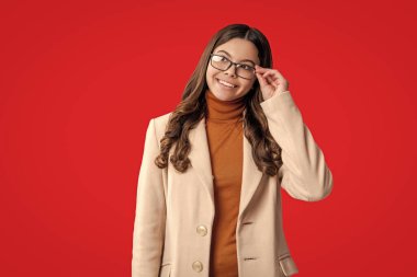 Sonbahar stil kızı. Moda ve şık bir öğrenci kız gülümsüyor. Gençler için sonbahar moda tarzı. Sonbahar modası. Sonbahar montlu kız öğrenci kırmızıda izole edilmiş. Genç kız gözlük takıyor, reklam yapıyor..