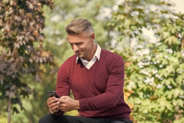 Adam sonbahar parkında telefon kullanıyor. Sıradan bir iş adamı gibi. İş adamı dışarıda telefonla mesajlaşıyor. İş iletişimi tarzı. Çevik iş. İnternet işi. İşadamı sonbaharda telefon kullanır..